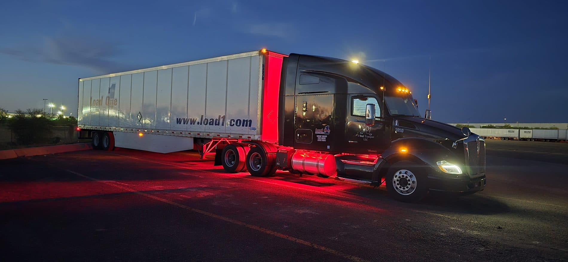 A Load One tractor-trailer staged at dusk with red running lights